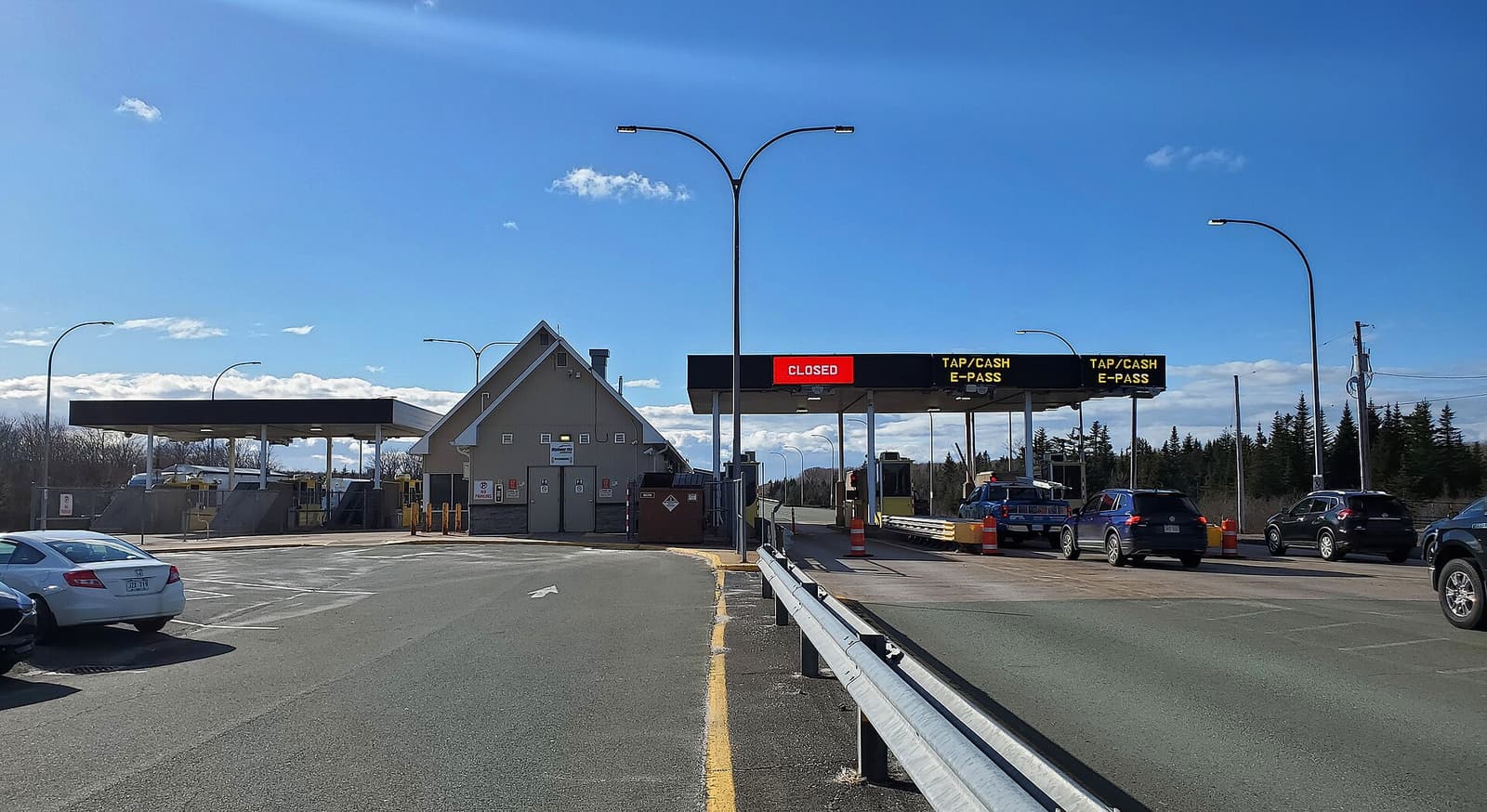 A highway toll plaza, its overhead signs marking the lanes that take a tap, cash or an electronic pass